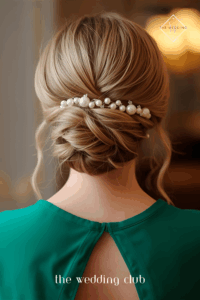 Low braided bun on long hair, emerald green cocktail dress, pearl hair accessory, elegant indoor wedding