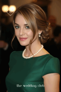 Medium hair styled into chignon with side part, fitted cocktail dress in emerald green, pearl necklace, formal wedding setting