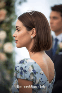 Sleek straight bob tucked behind ear, bold earrings showing, wedding ceremony backdrop